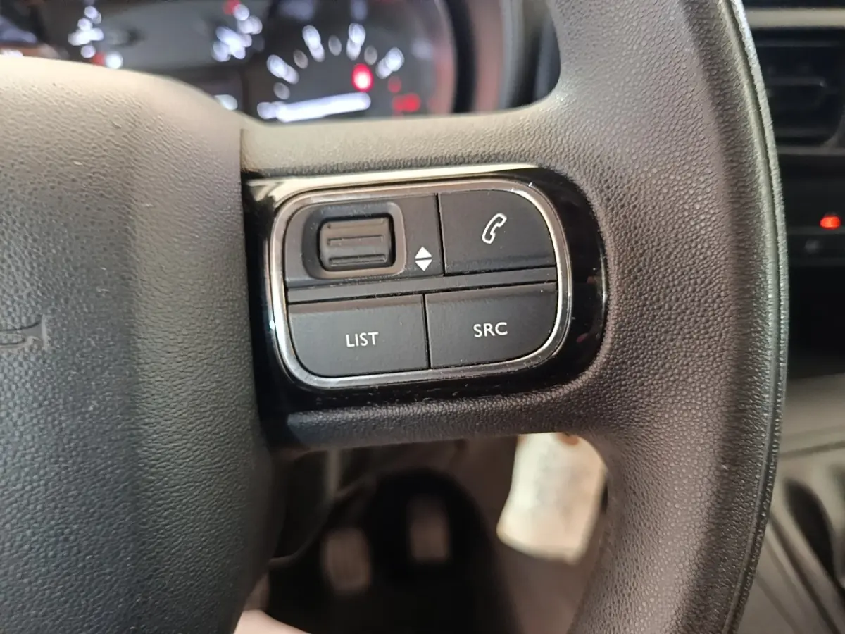 Gros plan sur les commandes noires multifonctions à gauche du volant du Citroën Berlingo 2020, intérieur sombre.