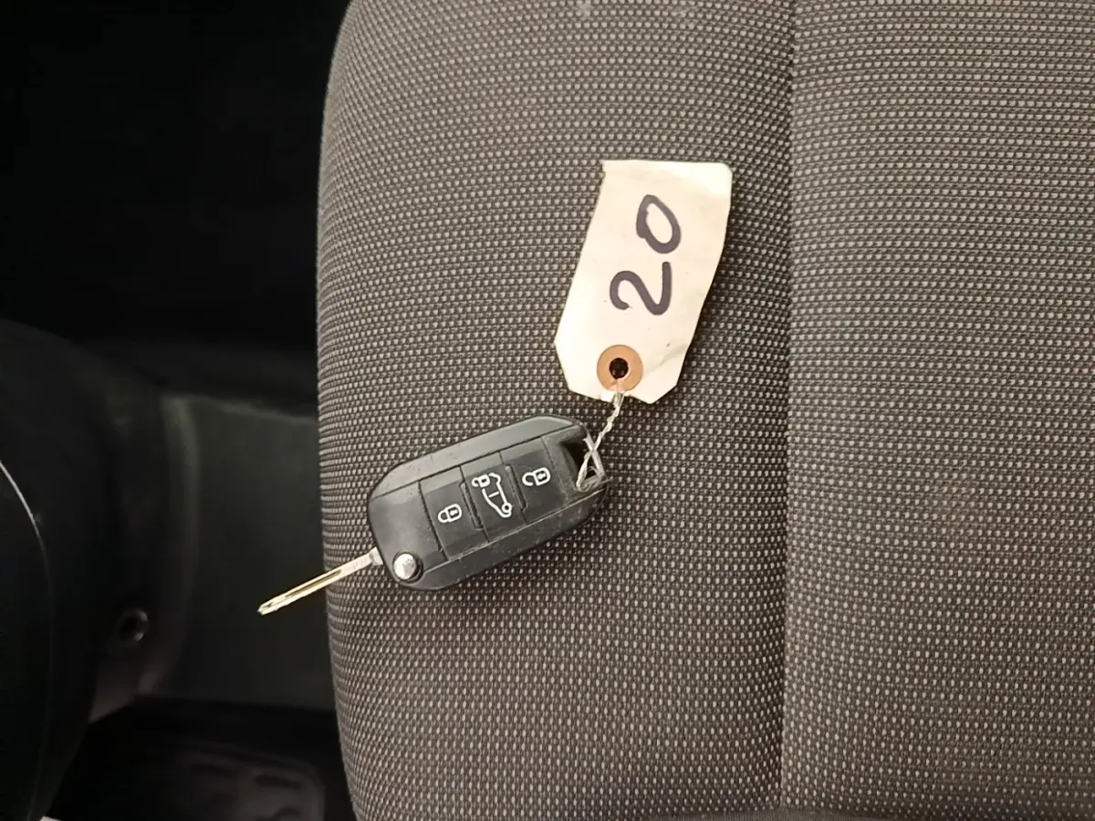 Clé de voiture noire avec étiquette "20" posée sur un siège tissu gris foncé à l'intérieur d'un Citroën Berlingo blanc.