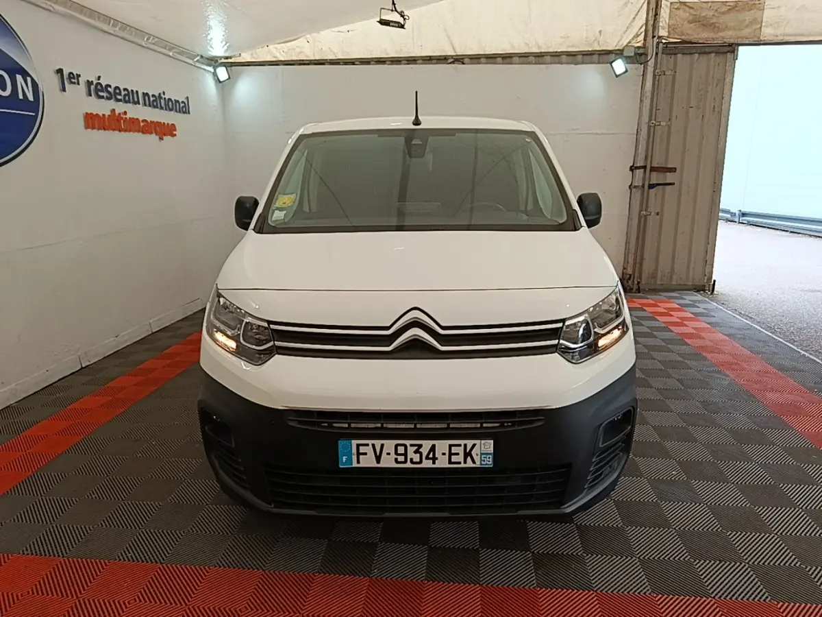 Vue de face d'un Citroën Berlingo XL blanc avec pare-chocs noir et feux allumés dans un garage.