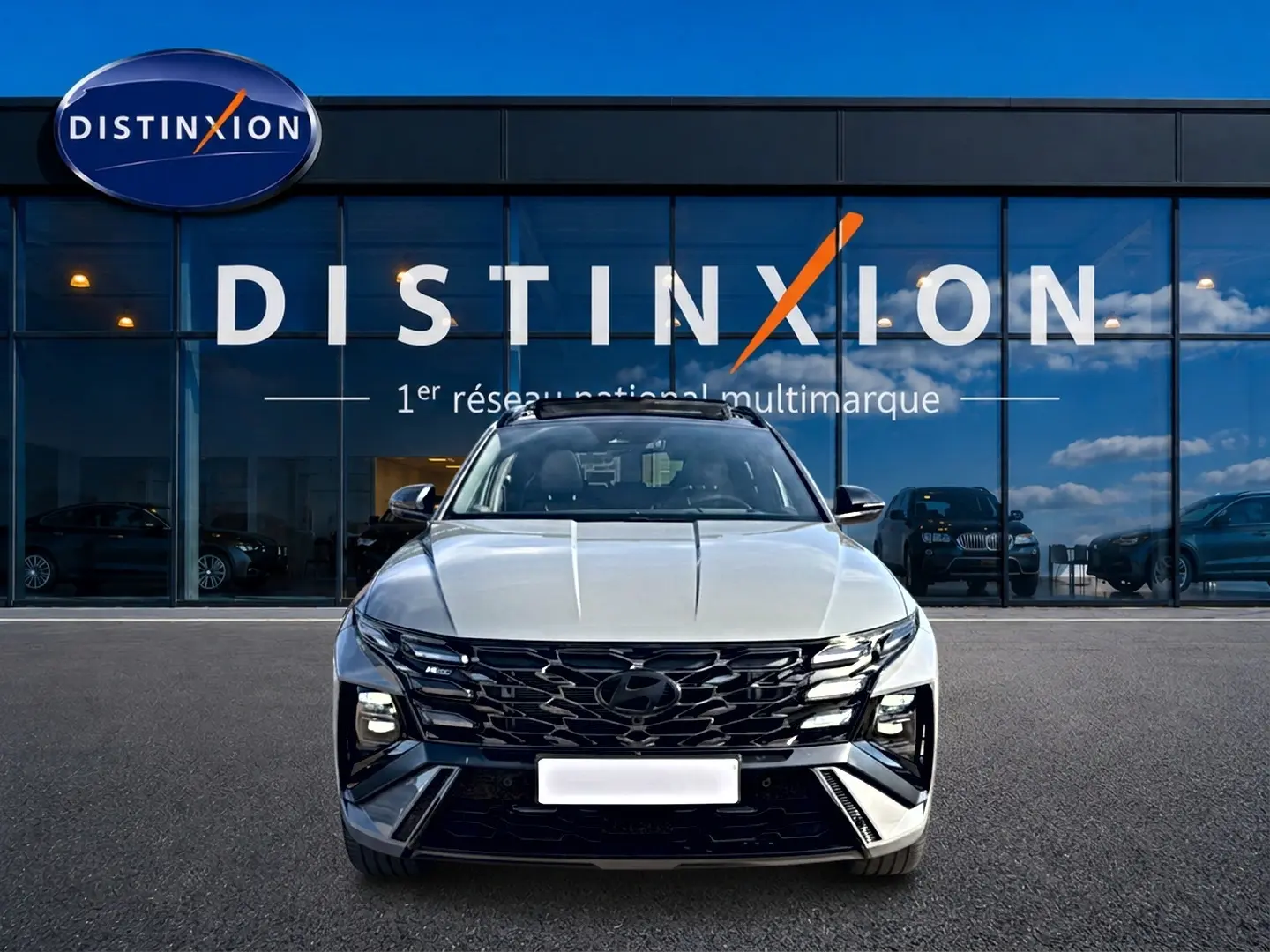 Vue avant du Hyundai Tucson 2026 gris shadow avec calandre noire et phares LED, devant une vitrine Distinxion.