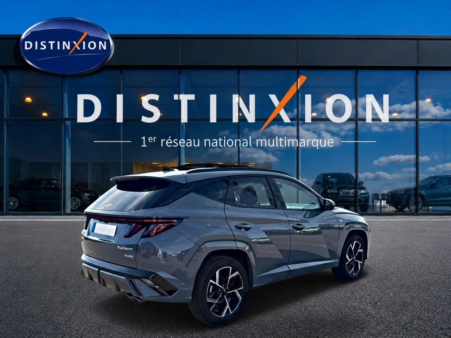Vue 3/4 arrière droite d'un Hyundai Tucson gris shadow avec jantes alu et feux arrière LED, devant un showroom Distinxion.