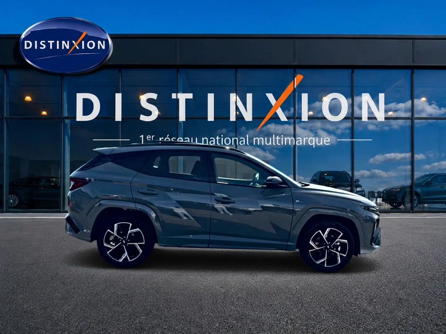 Hyundai Tucson 2026 gris shadow en profil gauche, avec jantes alu et calandre chromée visible devant un showroom Distinxion.