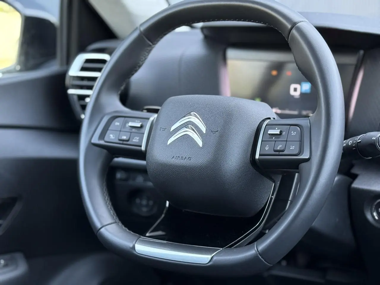 Gros plan sur le volant cuir noir du Citroën C4 X 2024 avec commandes intégrées et logo argenté central.