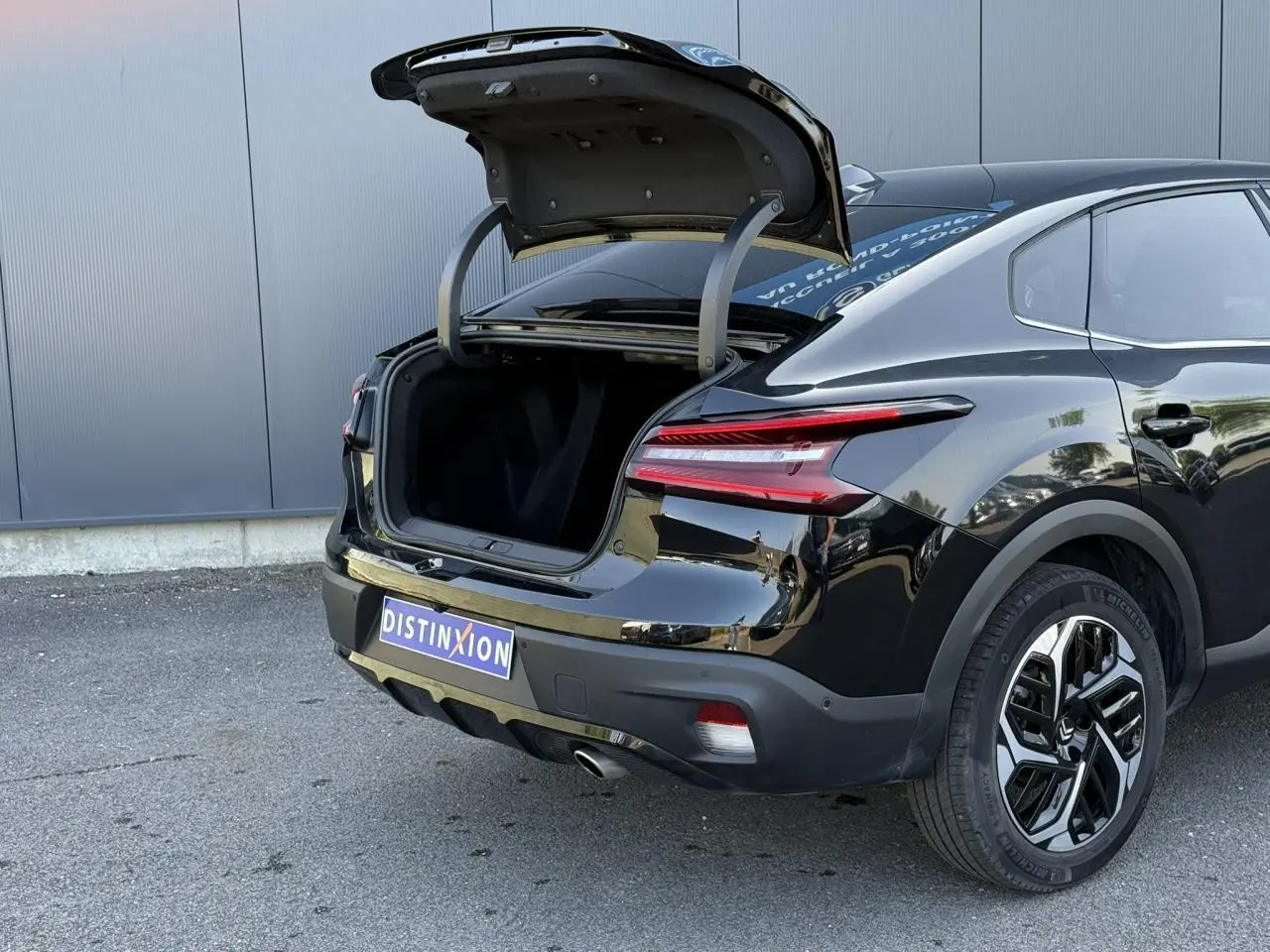 Vue 3/4 arrière droite d'une Citroën C4 X noire Perla avec coffre ouvert et jantes alliage diamantées.