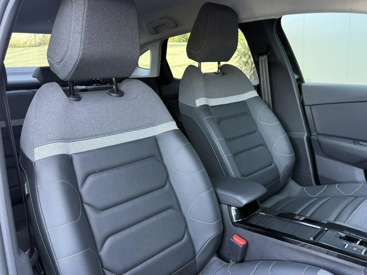 Vue rapprochée des sièges avant bi-matière gris et noir du Citroën C4 X 2024, avec accoudoir central.