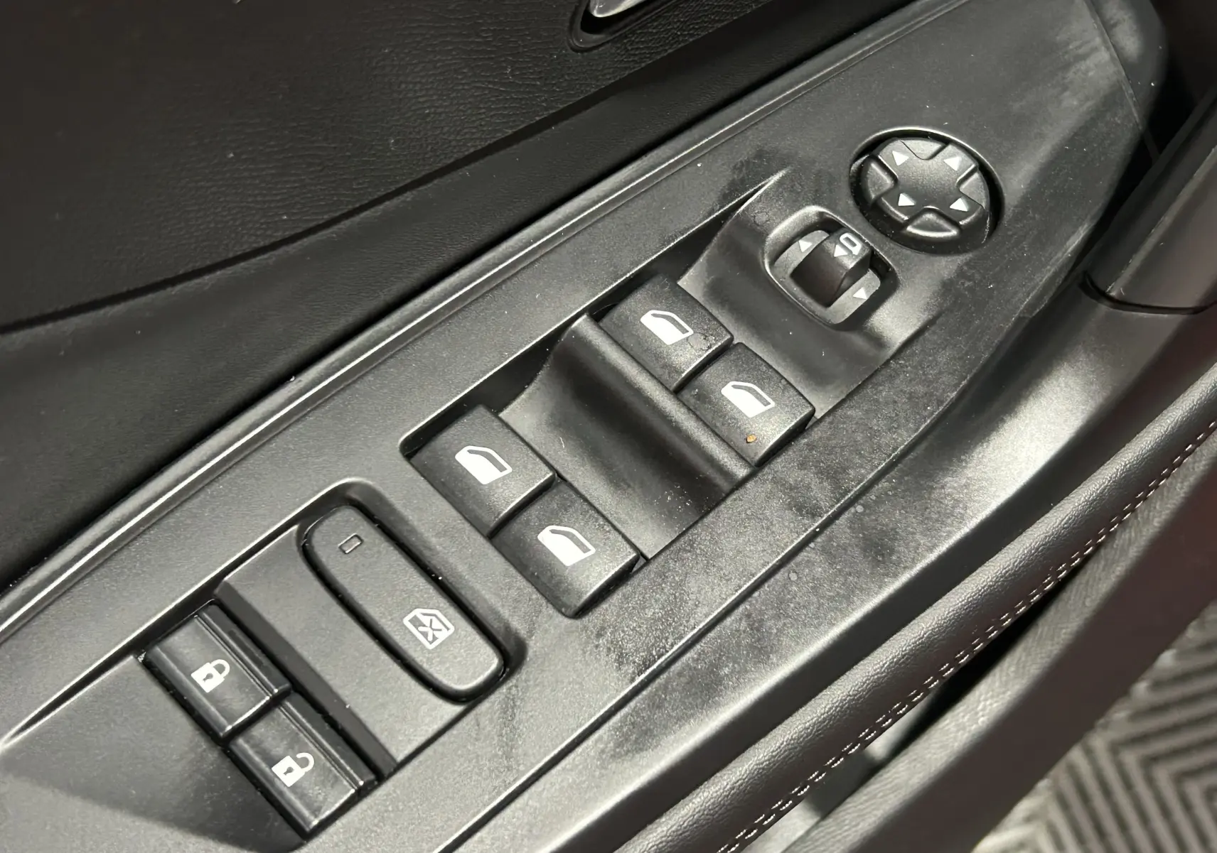 Gros plan sur les commandes des vitres électriques et rétroviseurs sur la porte côté gauche d’une Peugeot 308 rouge 2024.