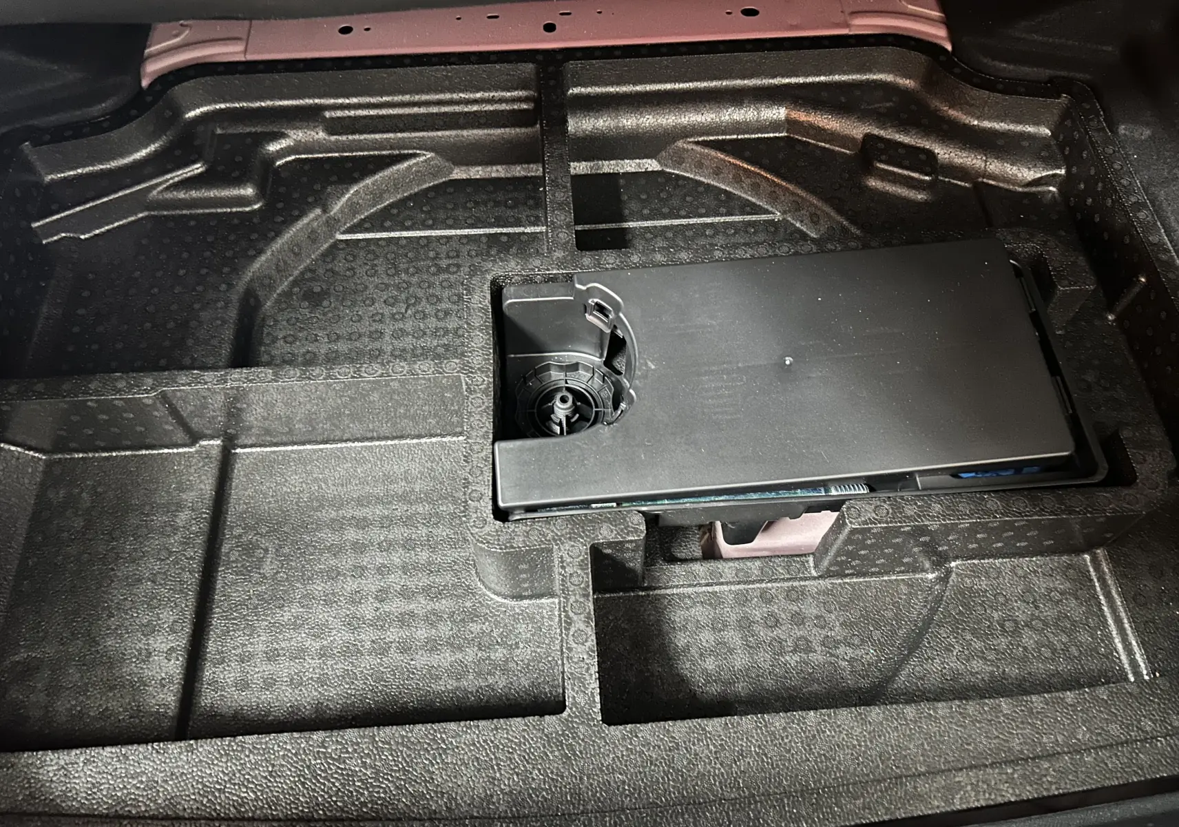 Vue rapprochée du compartiment de rangement sous le plancher du coffre de la Peugeot 308 rouge 2024.