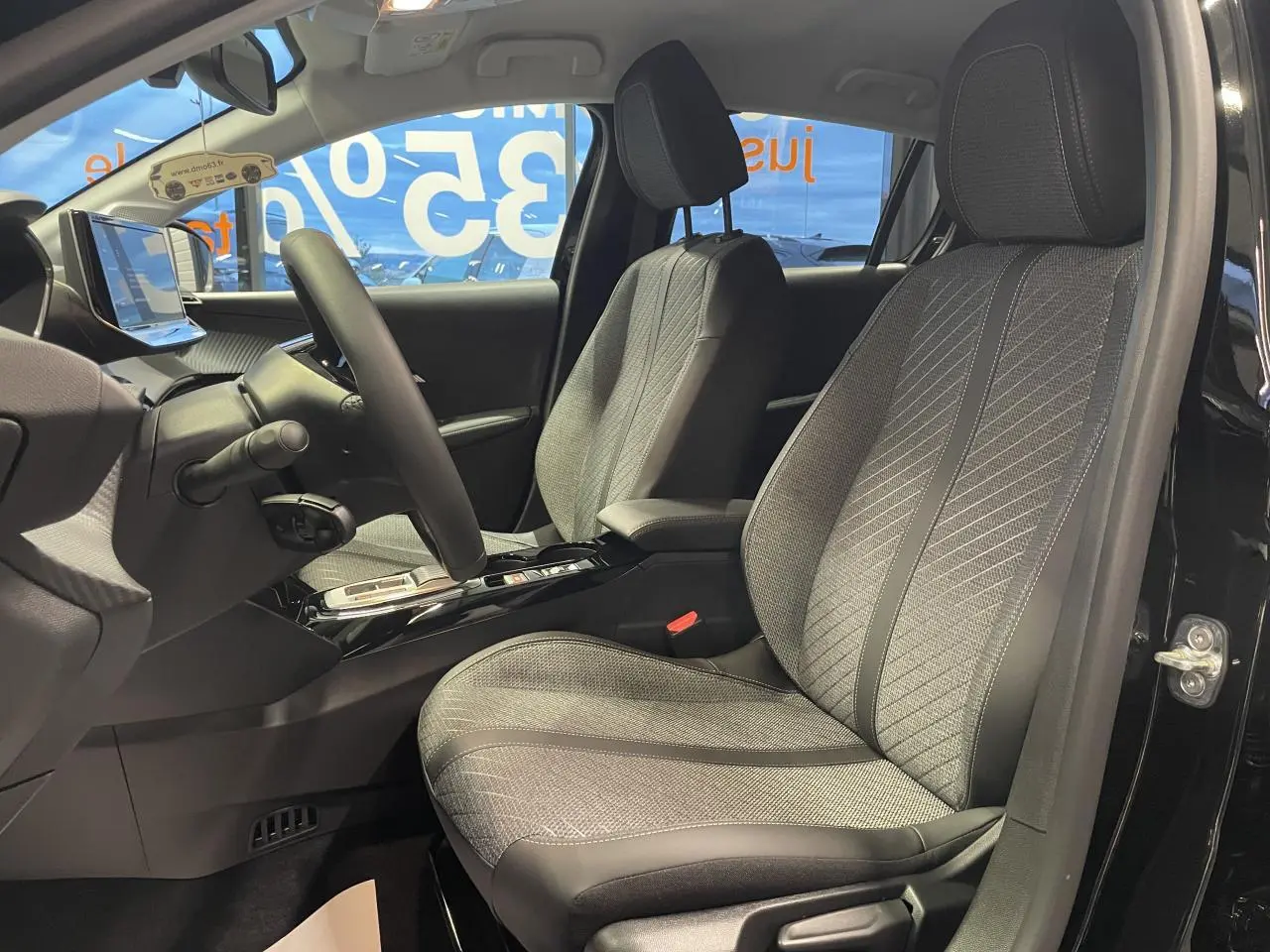 Intérieur avant de la Peugeot 208 noire, vue côté conducteur avec sièges tissu gris à motifs et volant compact cuir.