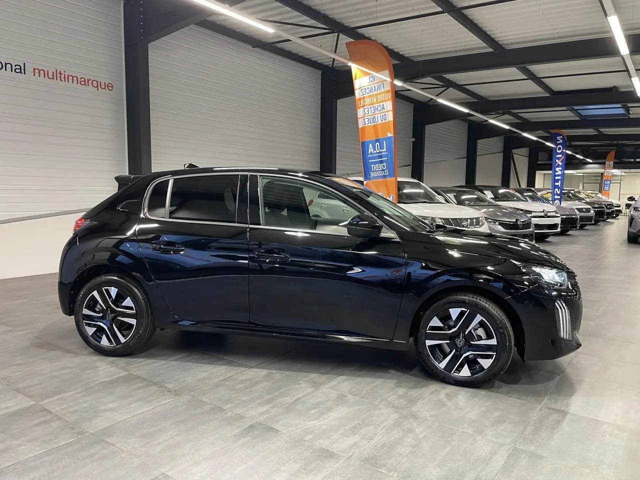 Peugeot 208 noire métallisée vue de profil côté gauche en intérieur avec jantes alliage bi-tons et vitres teintées.