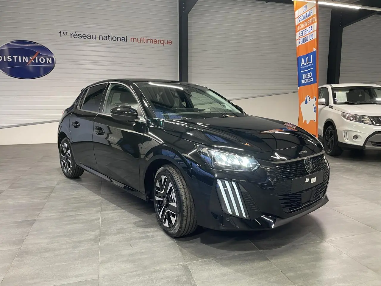 Peugeot 208 hybride noir métallisé vue 3/4 avant avec feux LED et jantes alliage bi-ton dans un showroom.