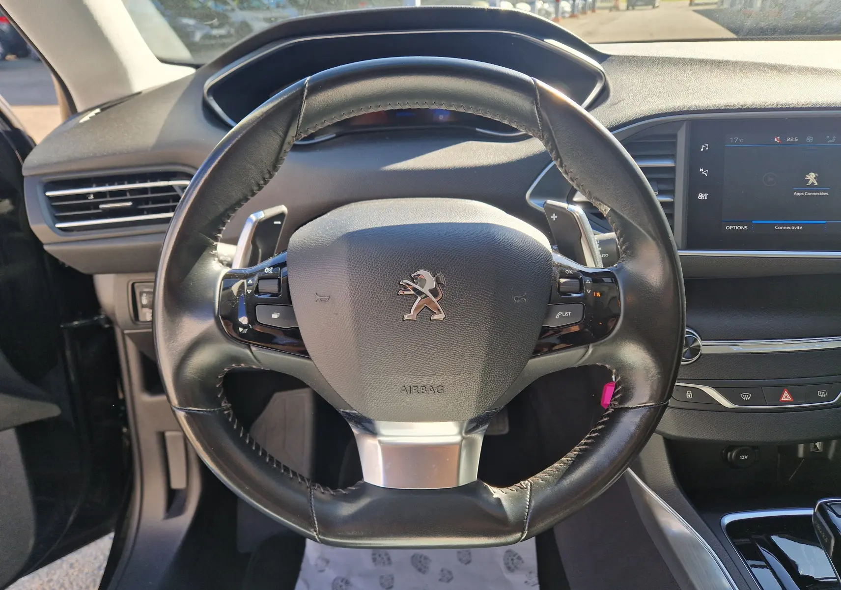 Vue rapprochée du volant cuir noir avec palettes de la Peugeot 308 SW 2021, tableau de bord et écran tactile visibles.