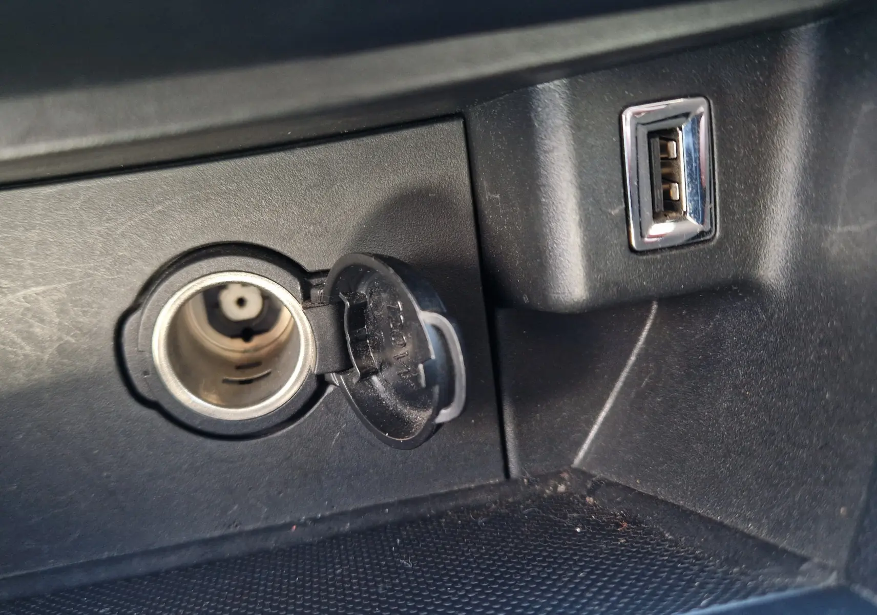 Prise allume-cigare ouverte et port USB visibles dans l'habitacle noir du Peugeot 308 SW 2021.