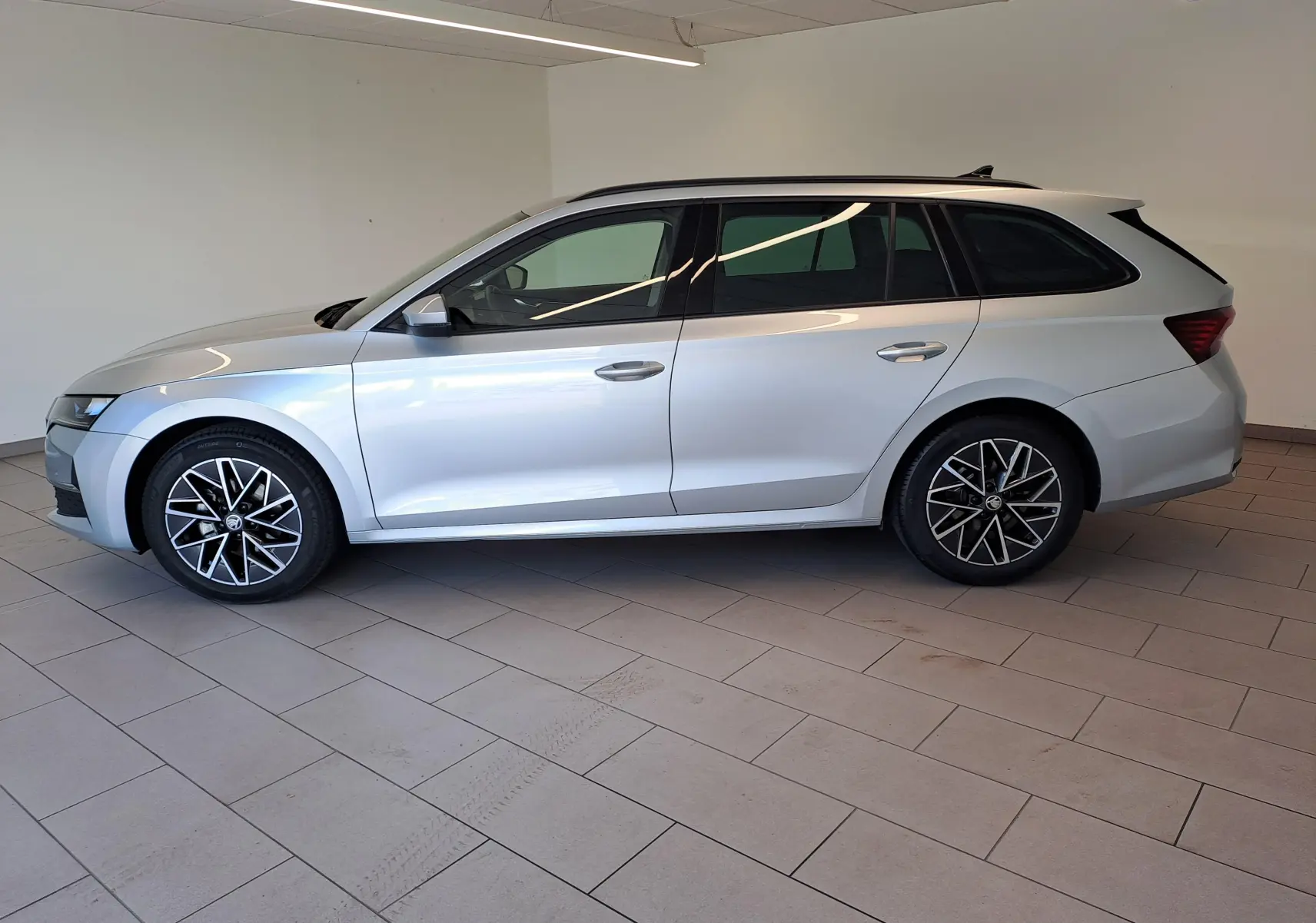 Vue de profil côté gauche d'une Skoda Octavia Combi gris argent 2025 avec jantes alliage noires polies et vitres surteintées.