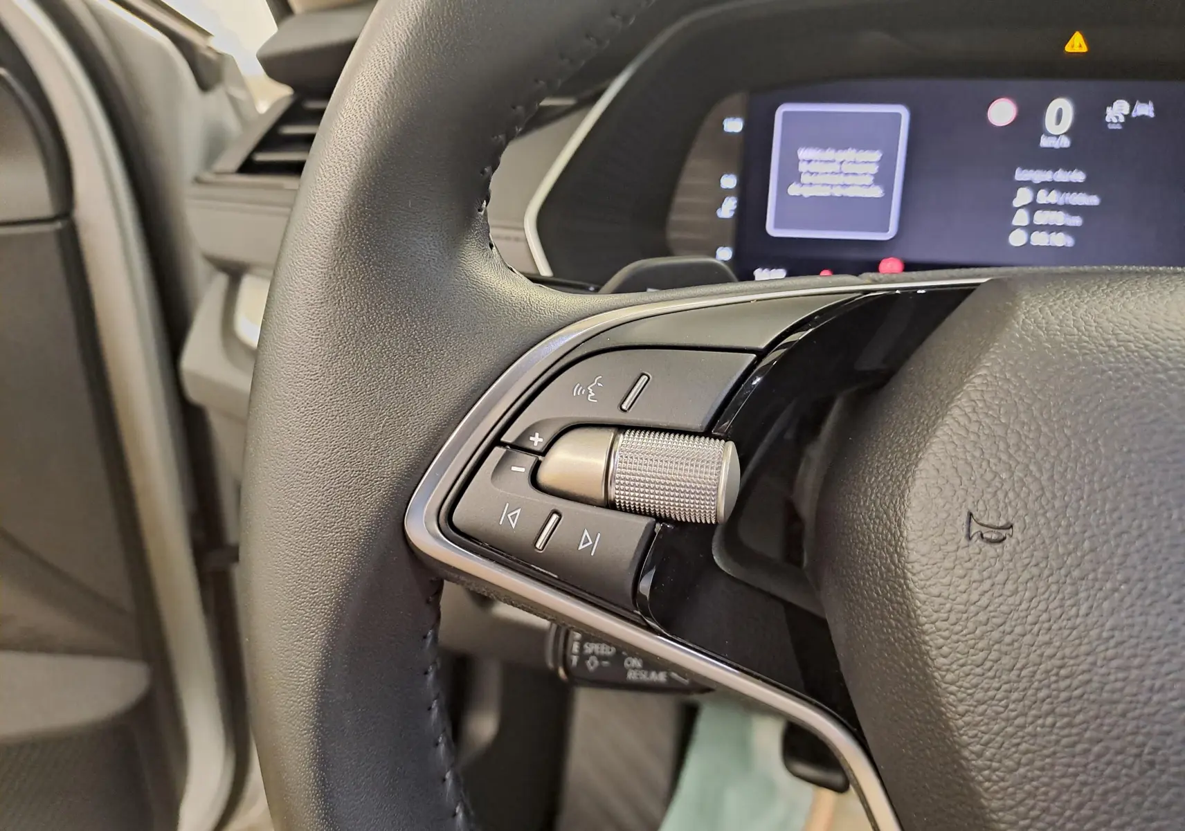 Gros plan sur les commandes gauche du volant noir de la Skoda Octavia Combi 2025, avec tableau de bord numérique en arrière-plan.