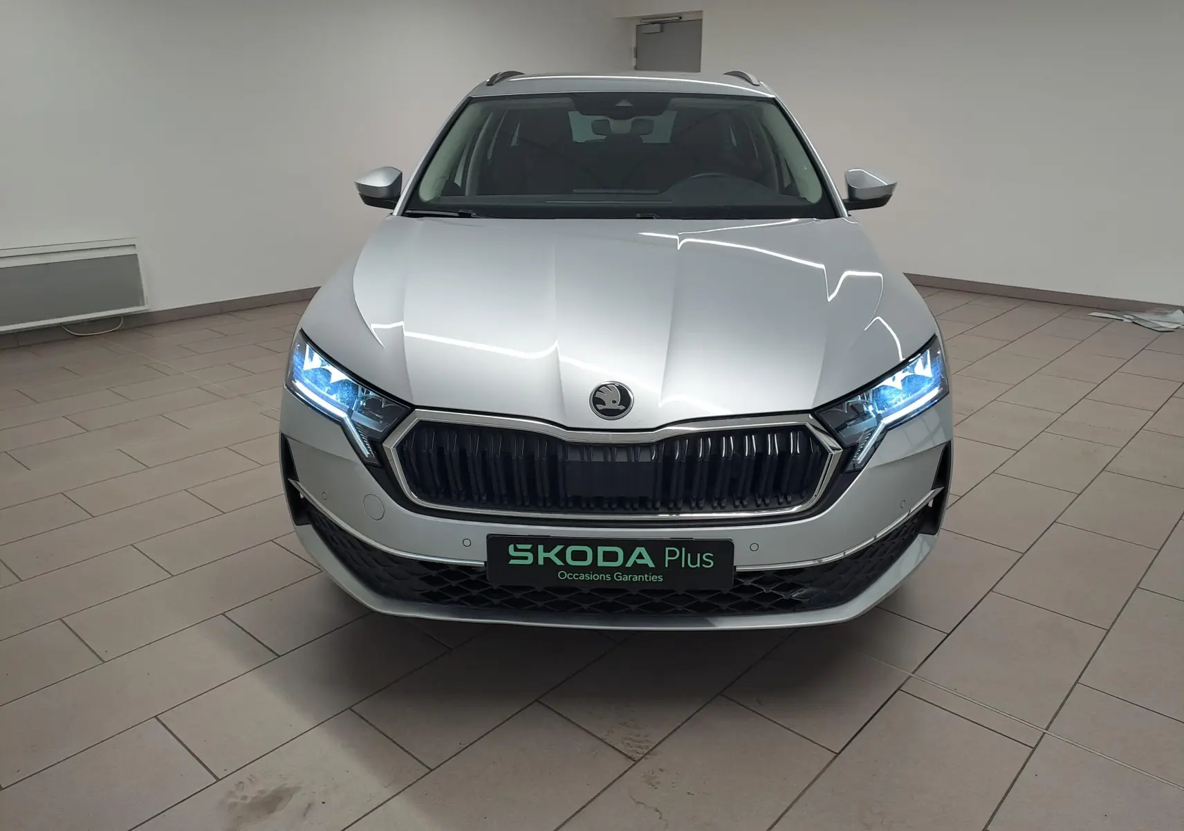 Vue frontale d'une Skoda Octavia Combi 2025 gris argent avec phares allumés et calandre noire distinctive.