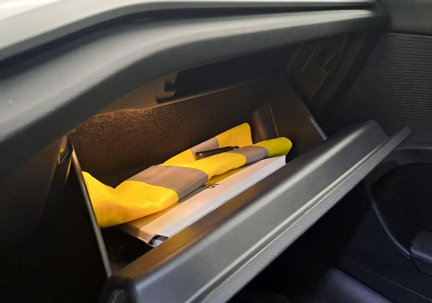 Gant de sécurité jaune dans la boîte à gants ouverte de la Skoda Octavia Combi 2025, intérieur noir.