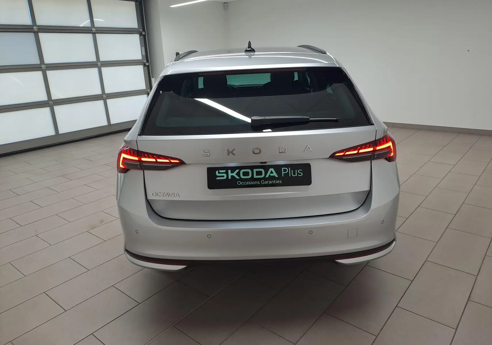 Vue arrière d'une Skoda Octavia Combi gris argent 2025 avec feux LED allumés dans un garage lumineux.