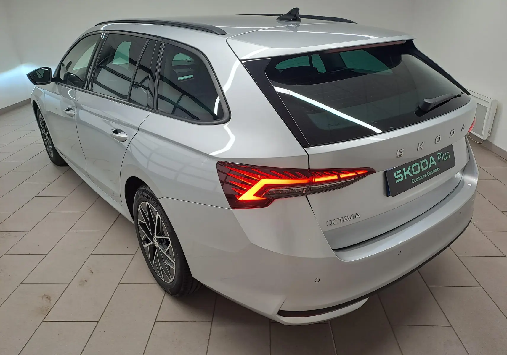 Vue 3/4 arrière droite d'une Skoda Octavia Combi gris argent avec feux arrière allumés et jantes alliage noires polies.