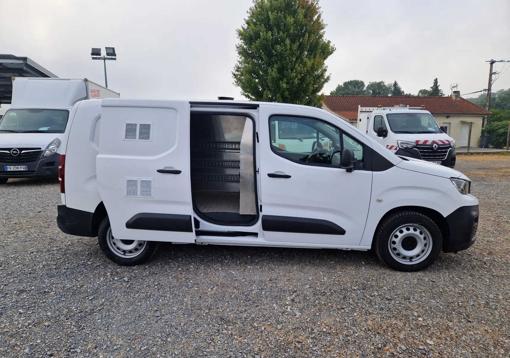 Vue de profil côté droit d’un Peugeot Partner blanc 2021 avec porte latérale coulissante ouverte montrant l’intérieur utilitaire.