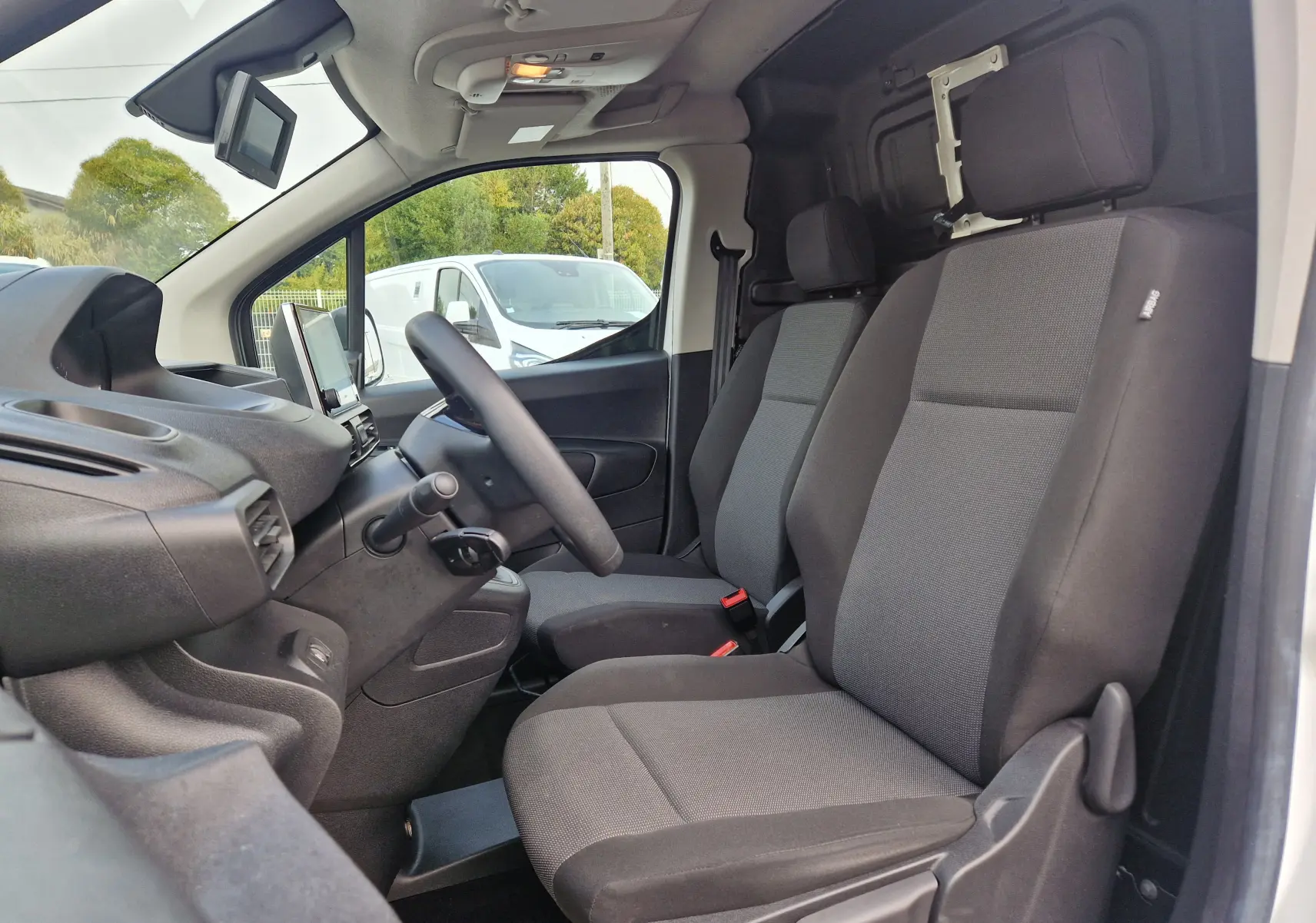 Vue intérieure côté conducteur du Peugeot Partner blanc 2021, montrant les sièges avant gris et le tableau de bord.