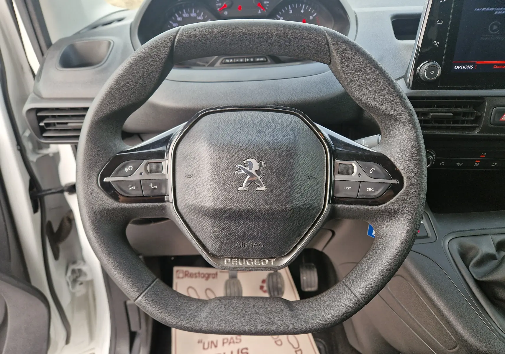 Vue rapprochée du volant noir du Peugeot Partner blanc 2021, avec commandes intégrées et tableau de bord en arrière-plan.