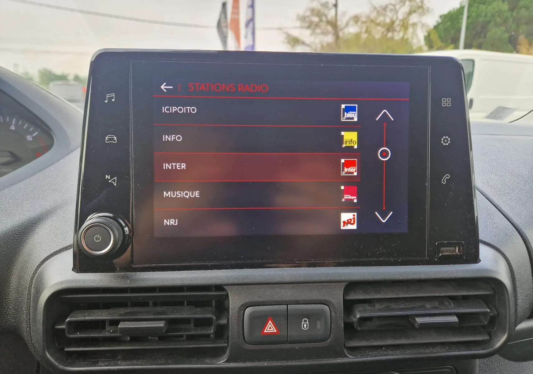 Écran tactile central du Peugeot Partner 2021 affichant la liste des stations radio, avec commandes et aérateurs visibles.