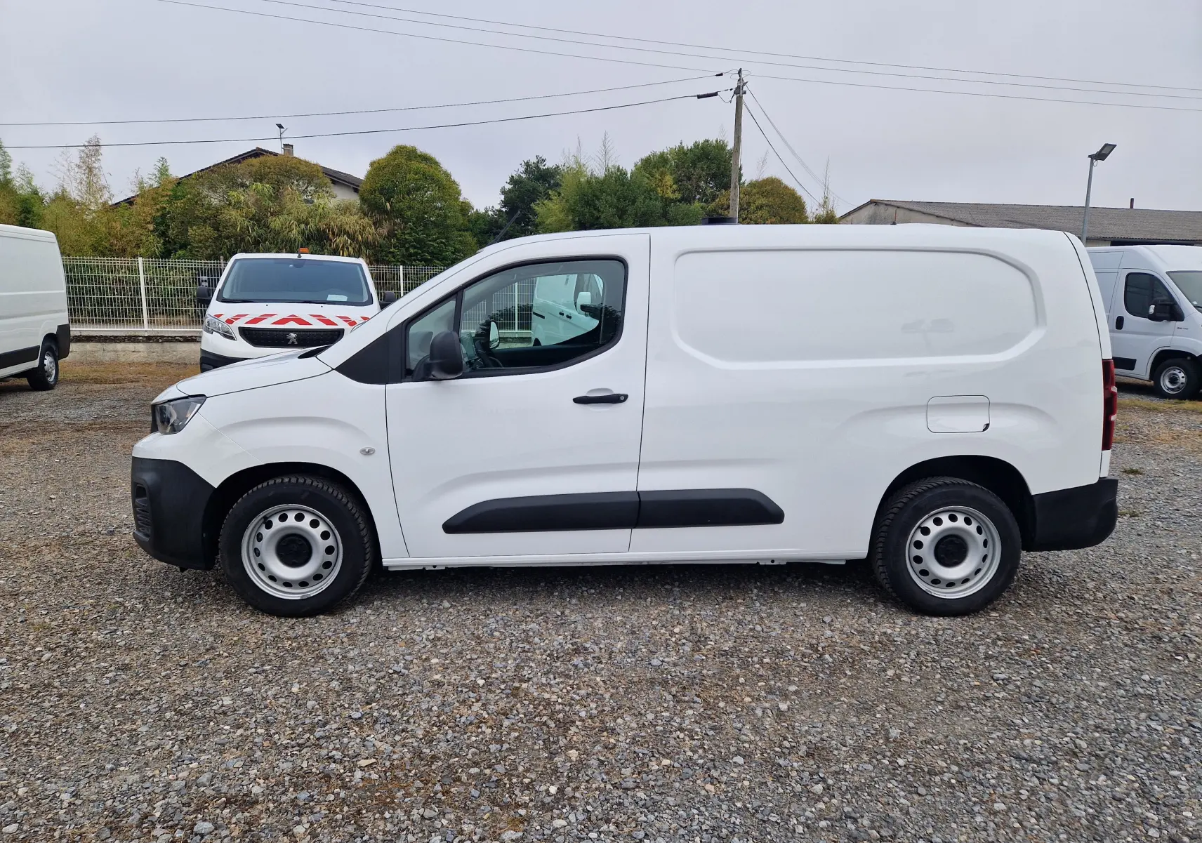 Vue de profil côté gauche d’un Peugeot Partner blanc 2021, version longue utilitaire avec protections noires sur les portières.