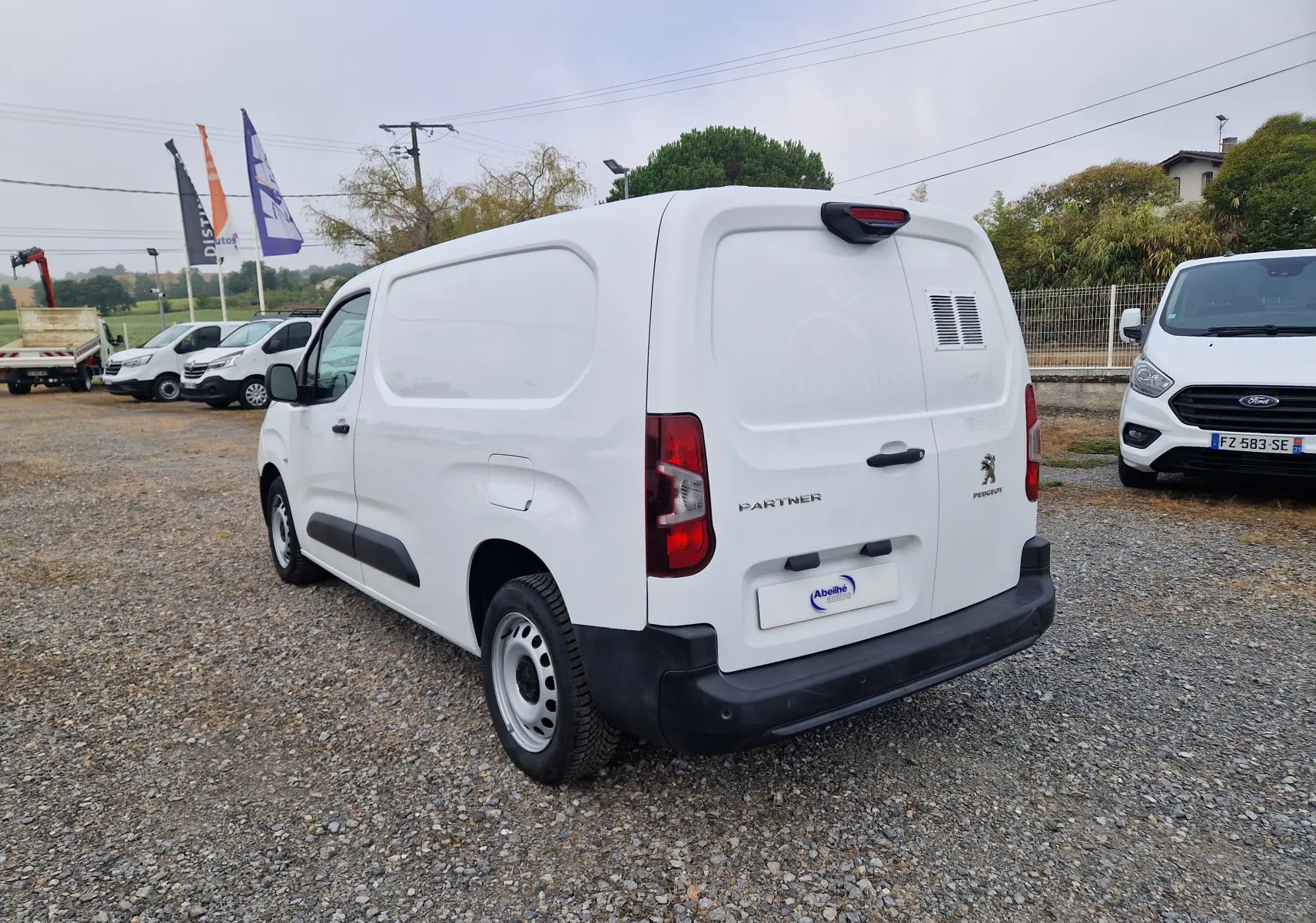 Vue 3/4 arrière droite d'un Peugeot Partner blanc 2021 utilitaire avec porte arrière ventilée et pare-chocs noir.