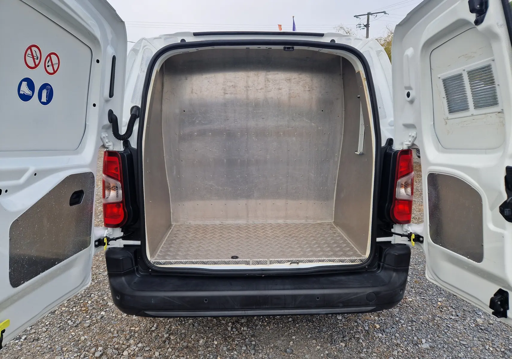 Vue arrière du Peugeot Partner blanc 2021 avec portes ouvertes, montrant l'espace de chargement métallique vide.