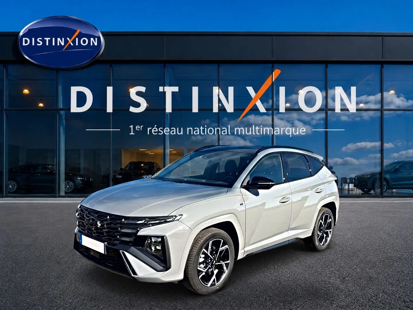 Vue 3/4 avant droite d'un Hyundai Tucson 2026 gris shadow avec jantes alu et calandre noire devant un showroom Distinxion.