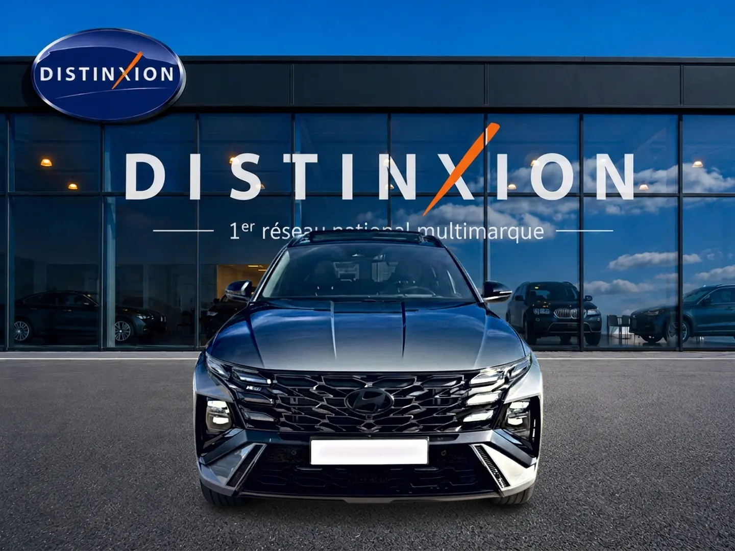 Vue avant d'un Hyundai Tucson 2026 gris shadow avec calandre noire et phares LED, devant une vitrine Distinxion.