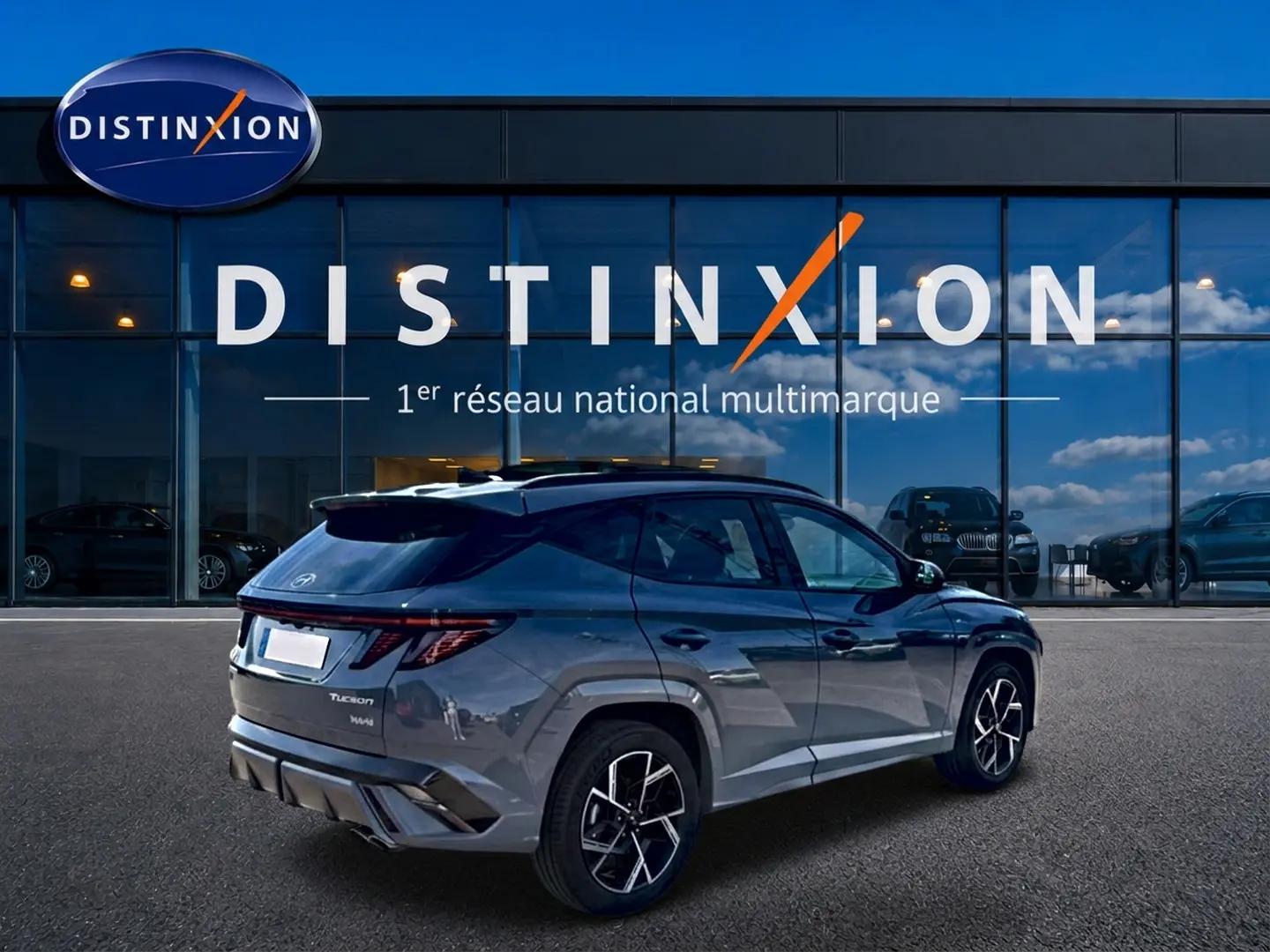 Vue 3/4 arrière droite d’un Hyundai Tucson gris shadow avec jantes alu et feux arrière LED, devant une vitrine Distinxion.