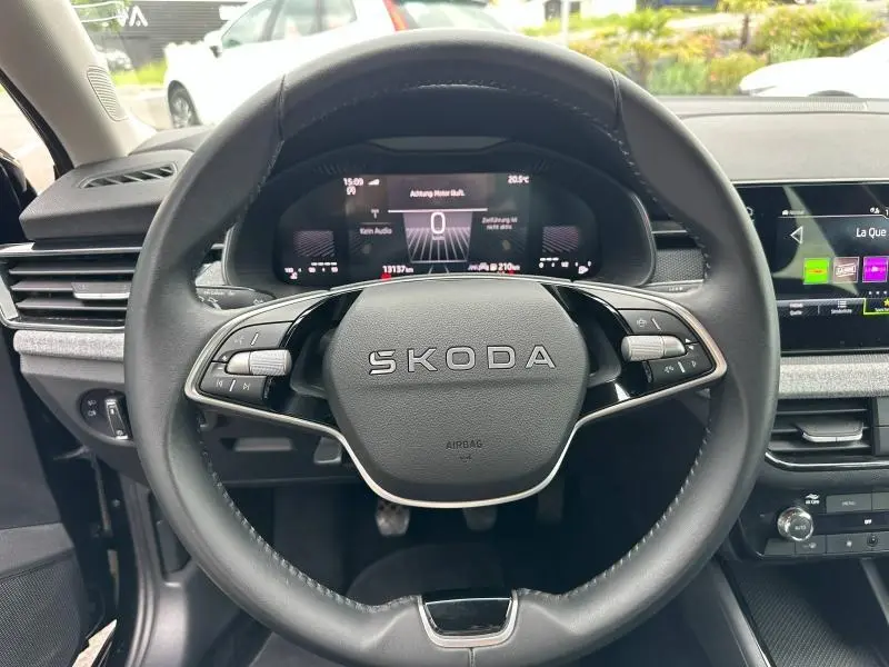 Vue rapprochée du volant cuir multifonction SKODA noir avec tableau de bord numérique et écran tactile à droite.