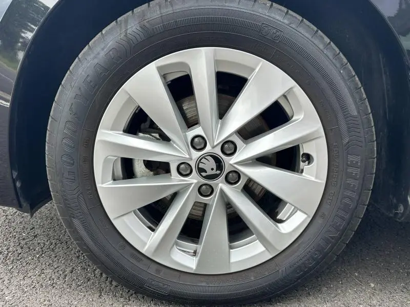 Gros plan sur la jante alu argentée avec logo ŠKODA au centre, montée sur pneu Goodyear, véhicule noir nacré visible en bordure.