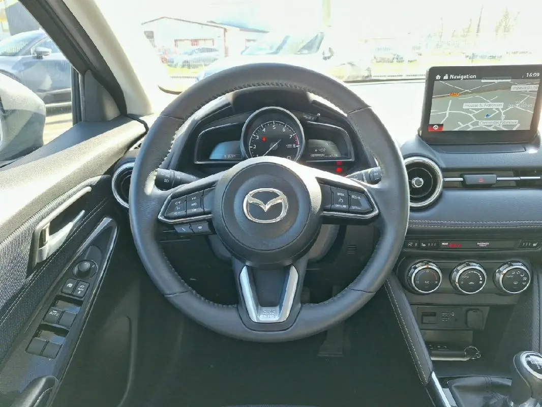 Vue intérieure centrée sur le volant cuir et tableau de bord avec écran tactile de la Mazda2 gris 2023.