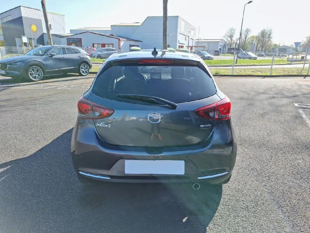 Vue arrière d'une Mazda2 gris métallisé 2023 avec feux rouges et lunette arrière teintée sur parking extérieur.
