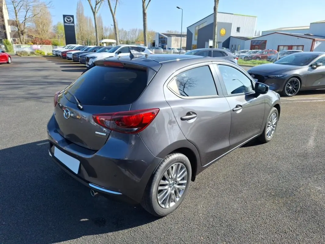 Vue 3/4 arrière droite d'une Mazda2 gris métallisé avec vitres surteintées et jantes aluminium sur parking.