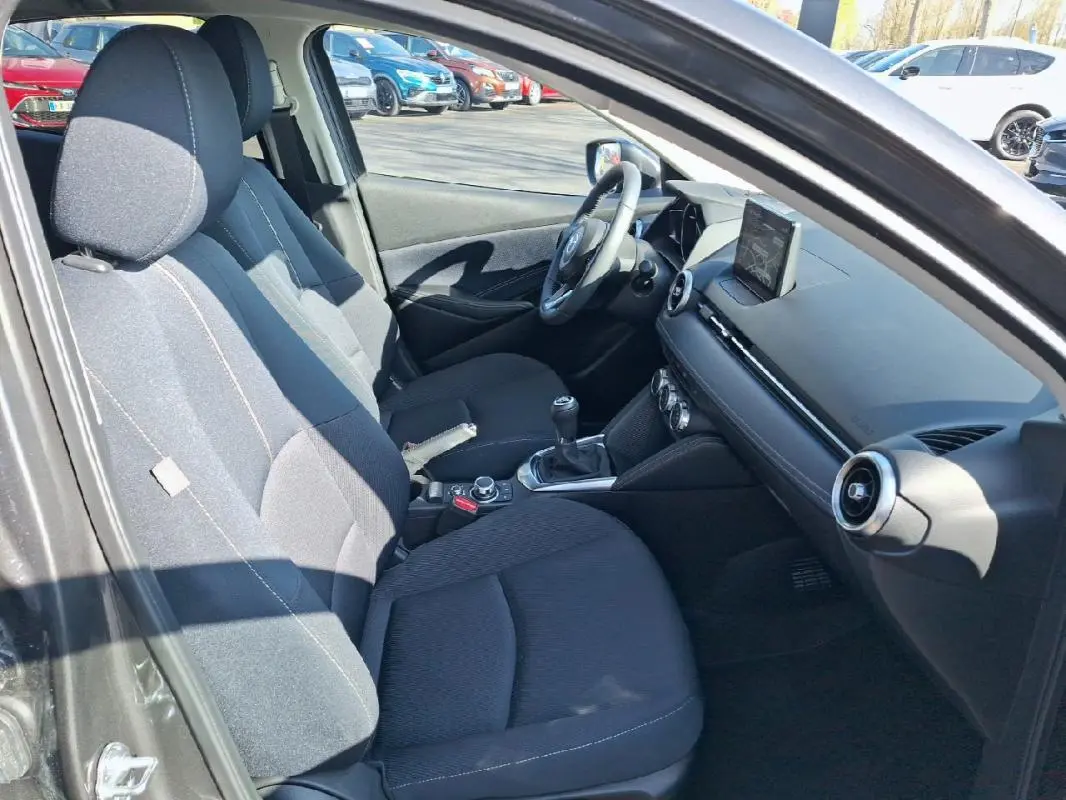 Intérieur avant de la Mazda2 2023, vue côté gauche, sièges noirs et tableau de bord avec écran tactile en relief.
