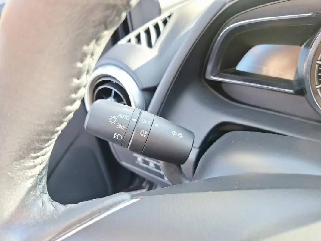 Gros plan sur le commodo des phares et clignotants à gauche du volant cuir dans l'habitacle gris de la Mazda2 2023.