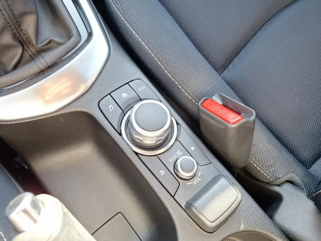 Gros plan sur la console centrale grise de la Mazda2 2023, avec molette de contrôle multimédia et frein à main.