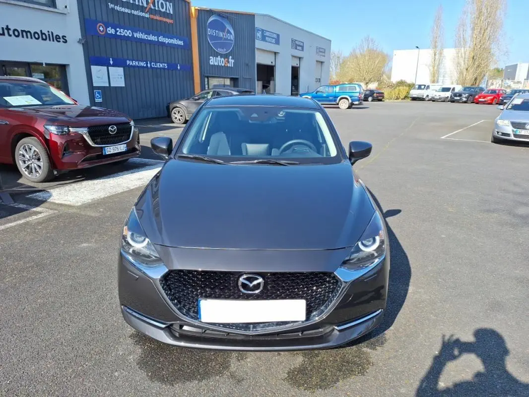 Vue frontale d'une Mazda2 gris métallisé 2023 avec calandre noire et phares LED circulaires visibles.
