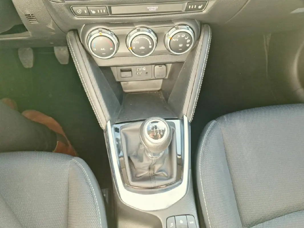 Vue plongeante sur la console centrale grise de la Mazda2 2023, avec levier de vitesse manuel et commandes de climatisation.
