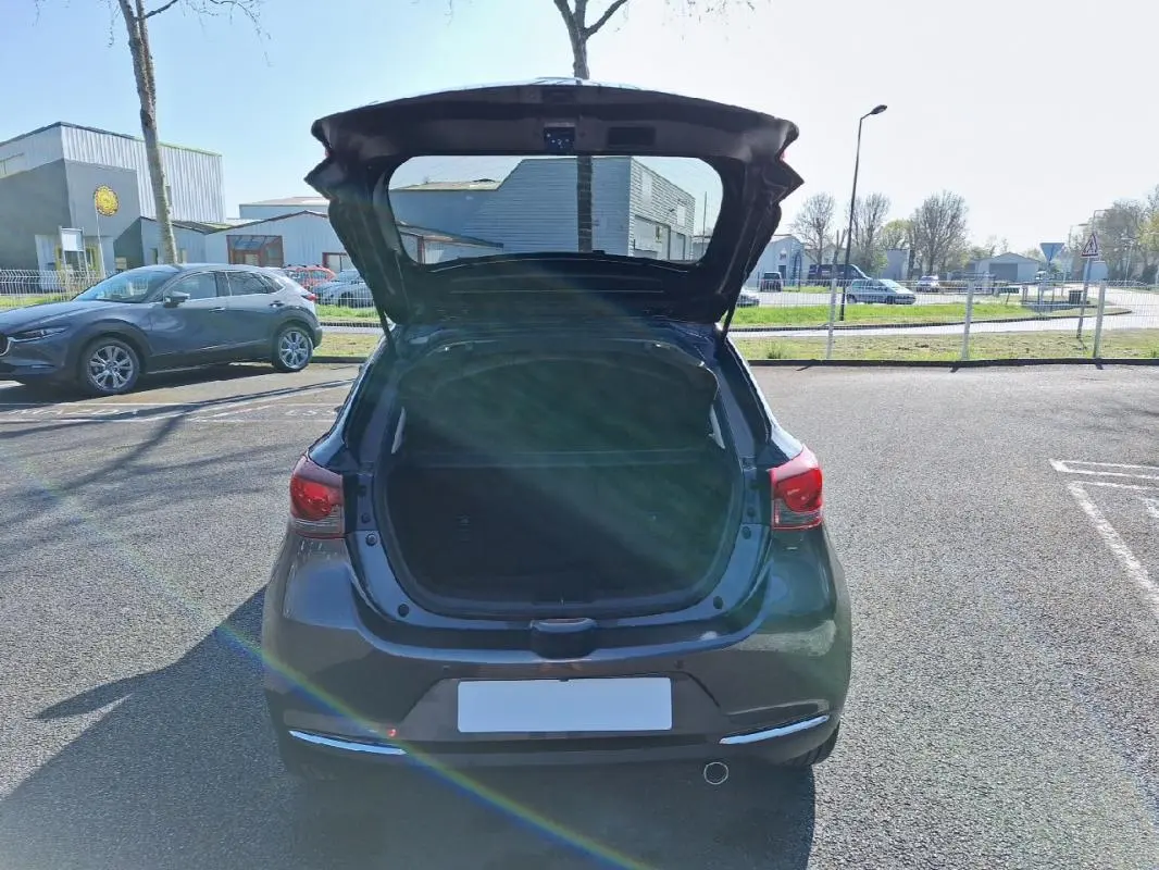 Vue arrière d'une Mazda2 gris avec coffre ouvert sur un parking ensoleillé.