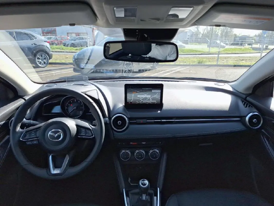 Vue intérieure avant du tableau de bord noir de la Mazda2 2023 avec écran tactile GPS et volant multifonctions cuir.