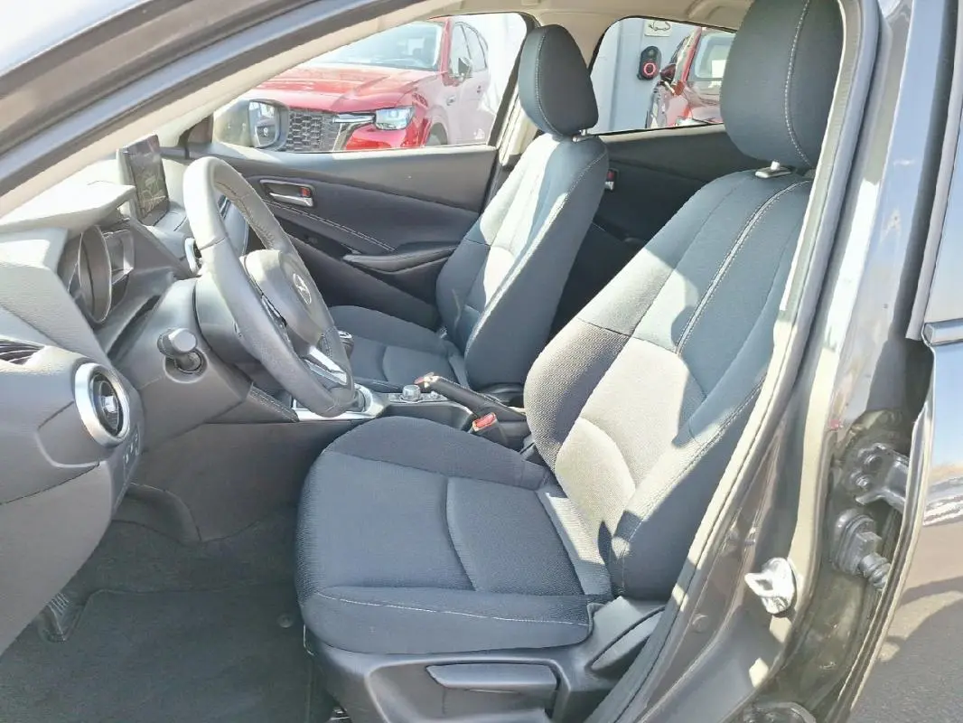 Intérieur avant de la Mazda2 gris 2023, vue côté conducteur montrant sièges tissu et tableau de bord moderne.