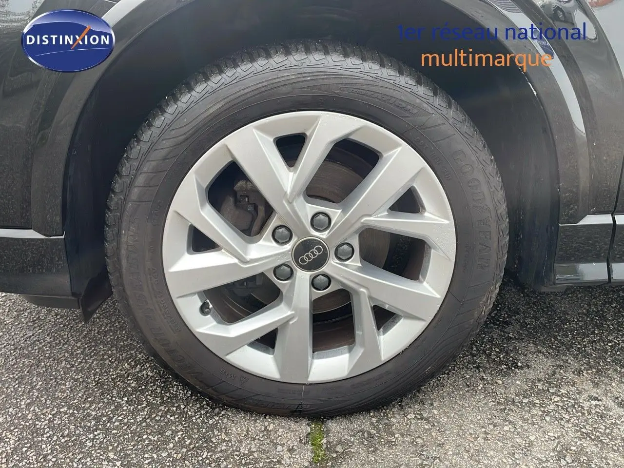 Gros plan sur la roue avant gauche d'un Audi Q2 noir mito metal, mettant en valeur la jante argentée à cinq branches.