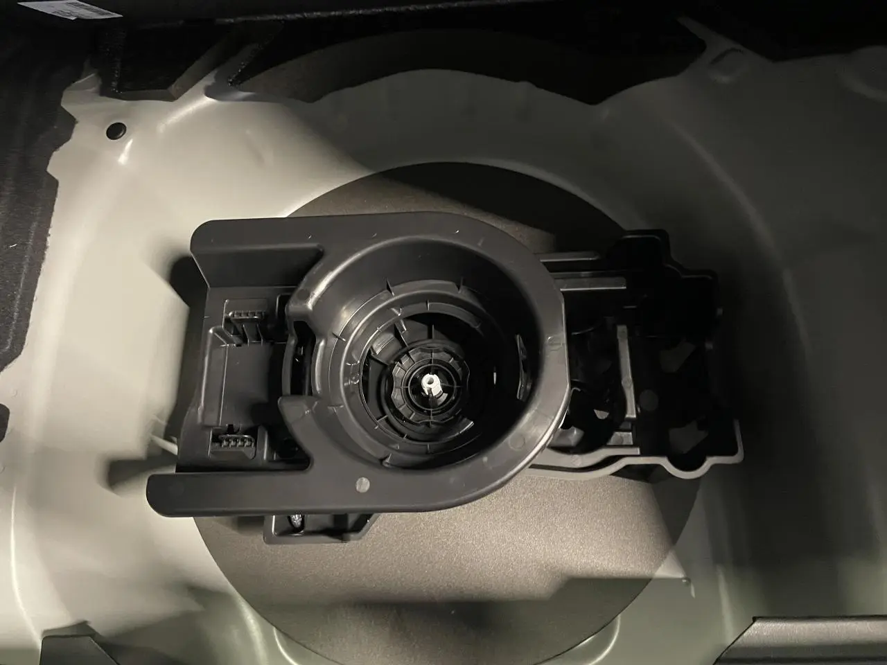 Gros plan sur le compartiment de rangement gris sélénium pour kit de dépannage pneumatique dans le coffre d'une Peugeot 208 hybride.