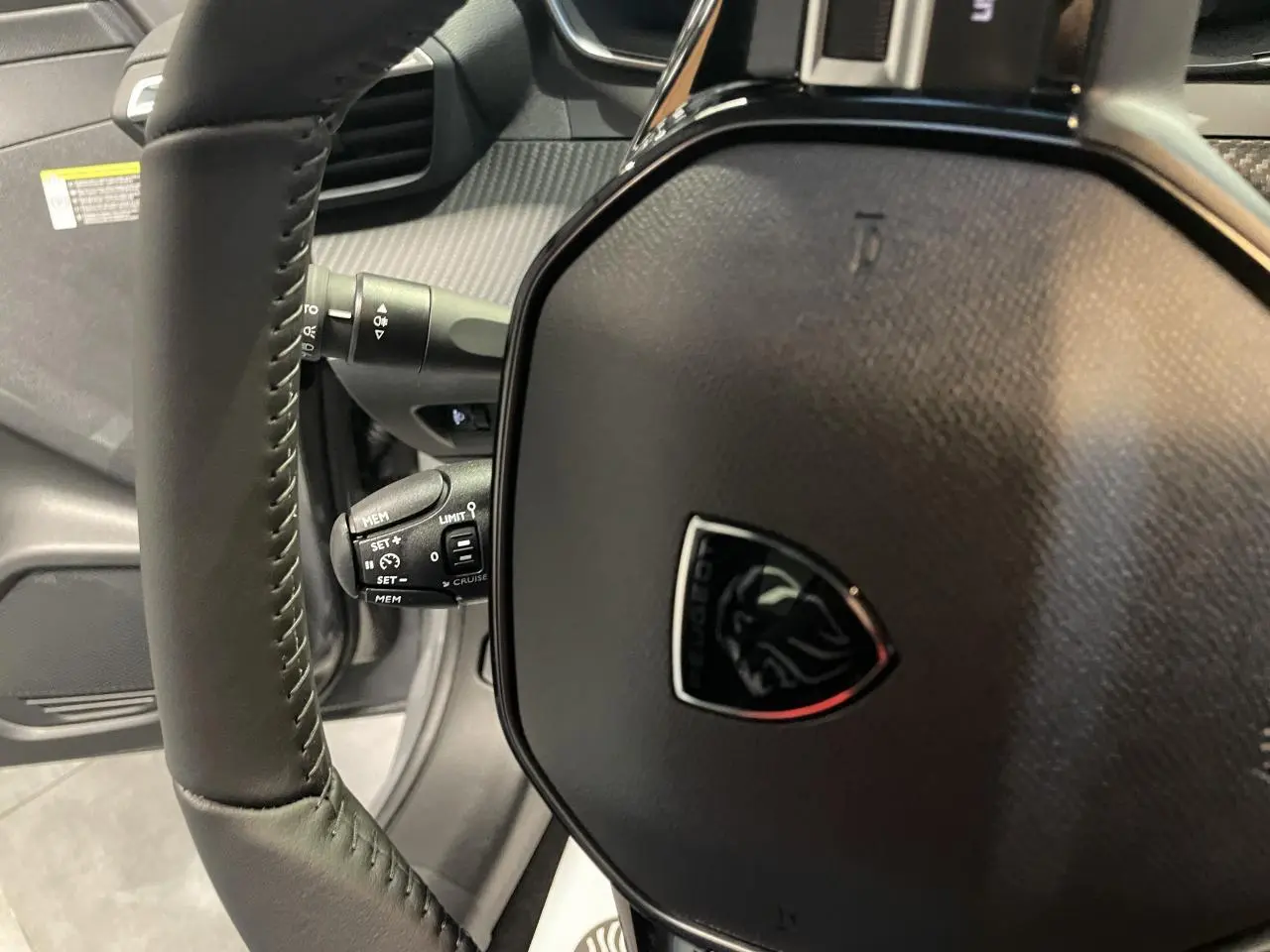 Gros plan sur le volant cuir noir de la Peugeot 208 2025 avec logo lion et commandes intégrées.