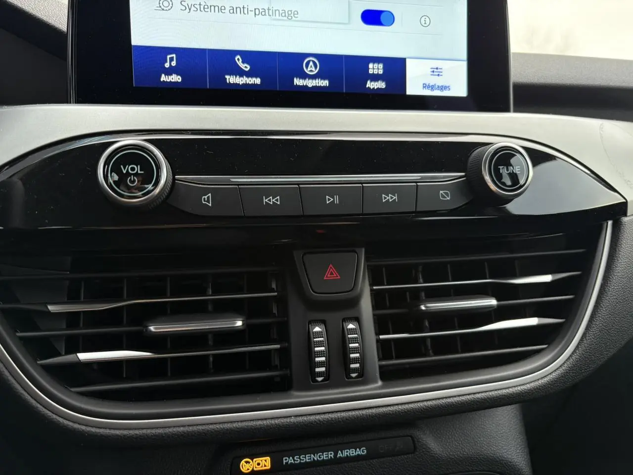 Vue rapprochée du tableau de bord noir du Ford Kuga 2024, avec commandes audio et écran tactile affichant le système anti-patinage.