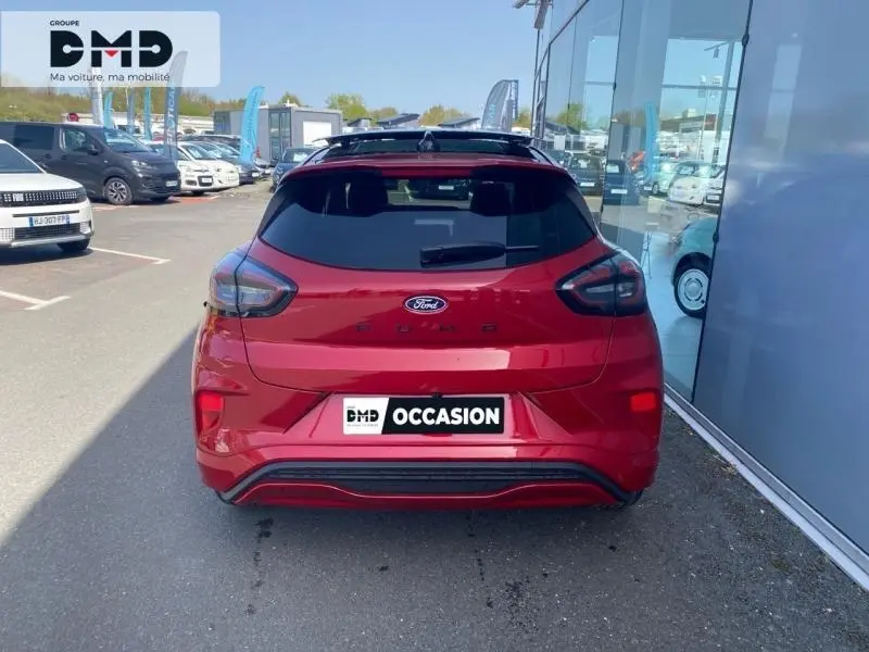 Vue arrière d'une Ford Puma rouge métallisée avec toit ouvrant panoramique, garée devant une vitrine ensoleillée.
